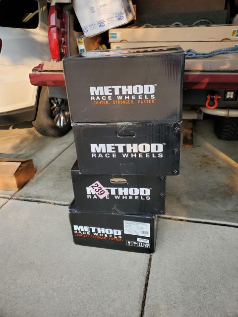 1996 Ford Bronco - Four boxes of Method Race Wheels are stacked on a driveway, with a vehicle's rear visible in the background.