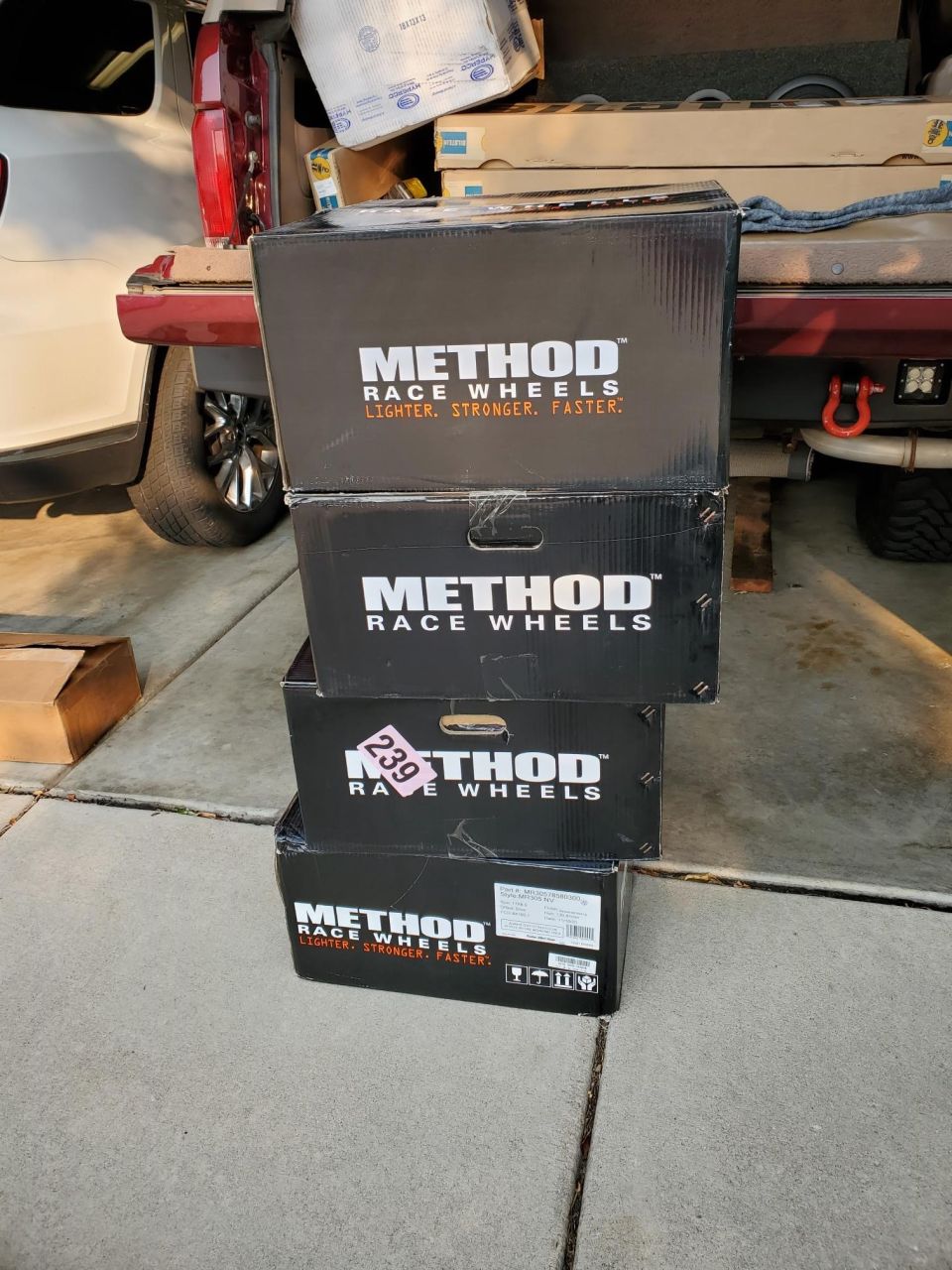 stack of Method Race Wheels boxes, some with "Lighter. Stronger. Faster." text, next to a vehicle's tailgate
