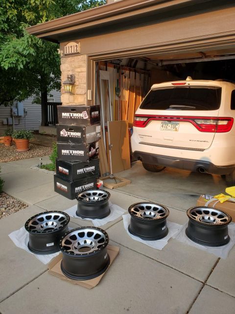 1996 Ford Bronco - Four new wheels are laid out on a driveway next to a white Dodge Durango parked in a garage.