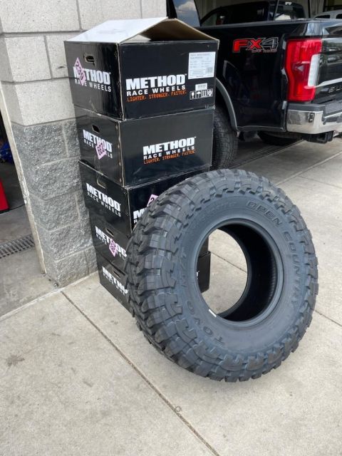 1996 Ford Bronco - New Method Race Wheels boxes and a Toyo Open Country tire are staged next to a Ford truck.