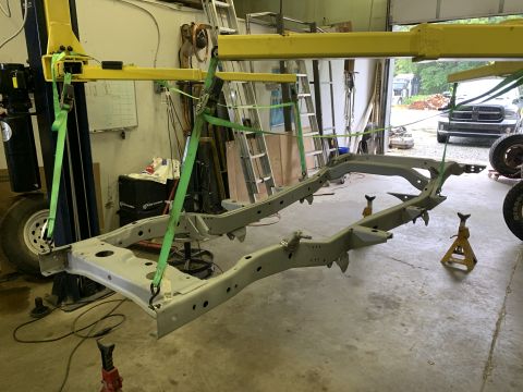 1979 Jeep CJ5 - A vehicle frame is being lifted by a yellow engine hoist in a workshop.
