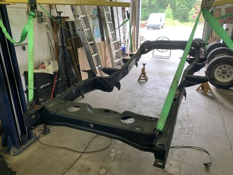 1979 Jeep CJ5 - The frame of a Jeep CJ is being worked on in a garage, with a white van visible outside.