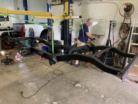1979 Jeep CJ5 - A Jeep CJ5 frame is being worked on in a garage, suspended by a yellow lift.