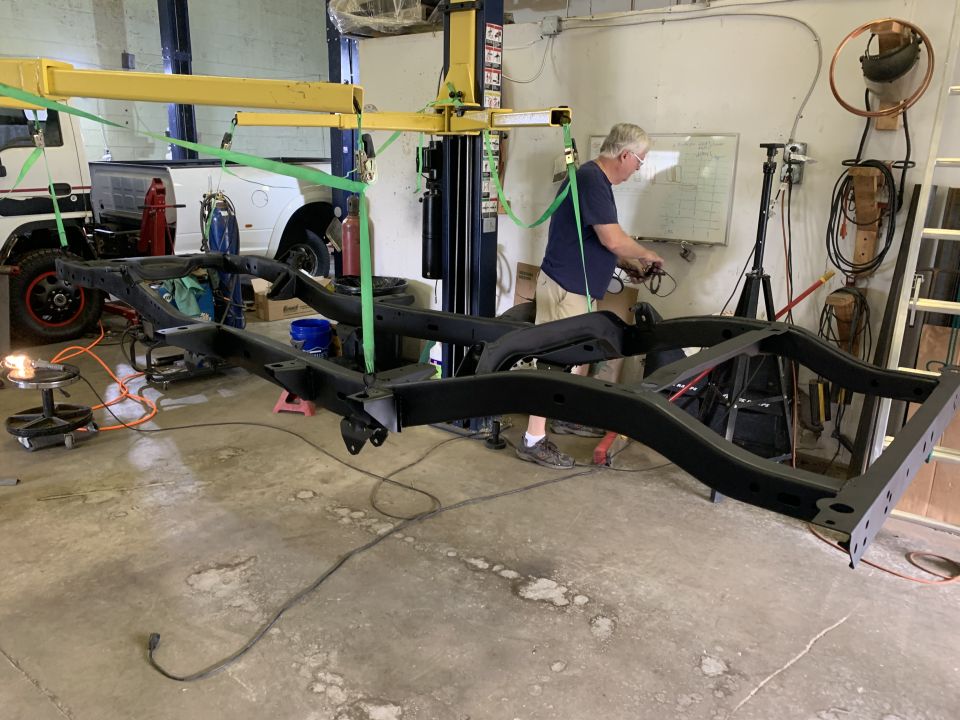 Jeep CJ5 frame suspended by a lift in a workshop