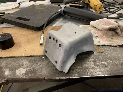 1979 Jeep CJ5 - A metal bracket and a grease gun sit on a workbench next to a power tool.