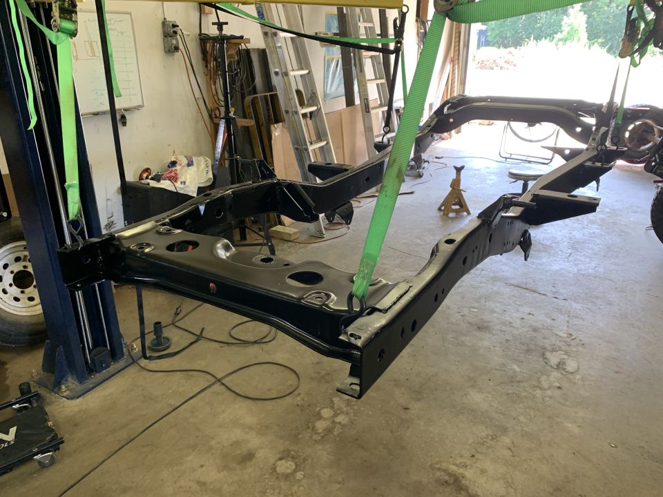 Vehicle frame suspended on lift, undergoing restoration