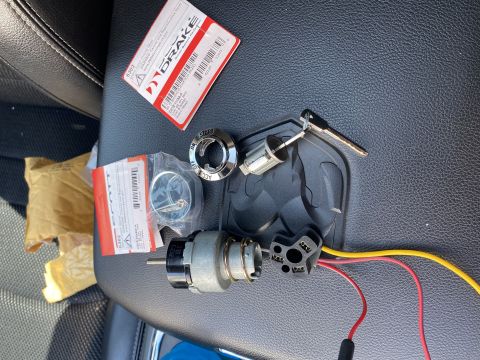 1976 Ford Bronco - Ignition switch components, including a lock cylinder and key, are laid out on a dark surface with packaging from Drake packaging visible.