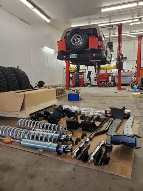 1996 Ford Bronco - A Ford Bronco is suspended on a lift with a collection of suspension components spread across the garage floor.