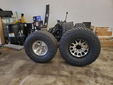 1996 Ford Bronco - Two large off-road tires and wheels are displayed in a garage setting, with various automotive parts and storage containers in the backgrou…