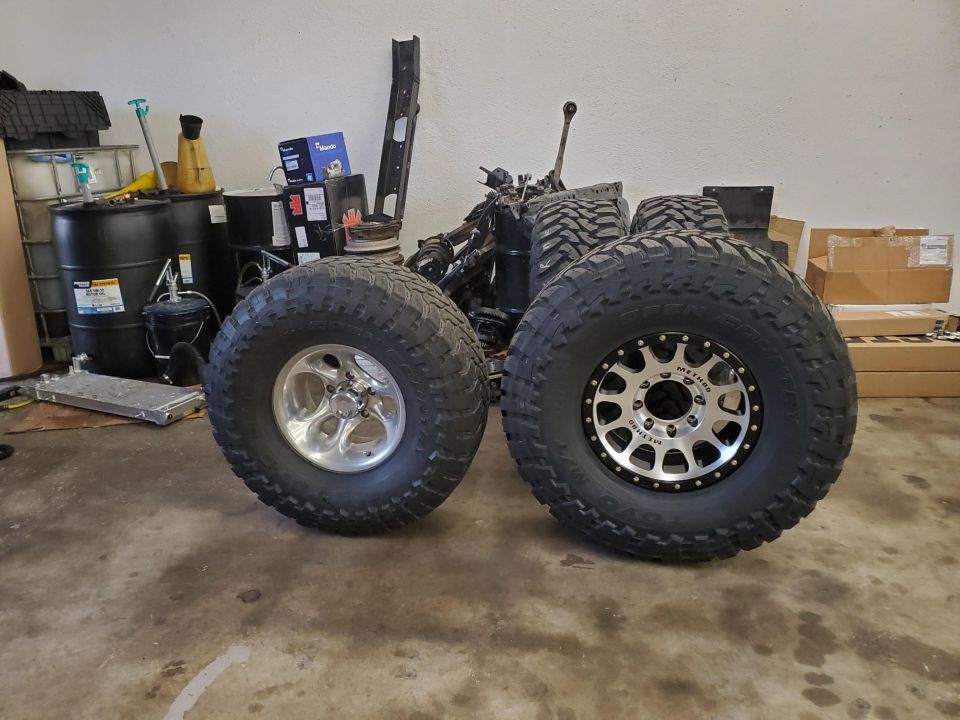 Two large off-road tires and wheels, one with a chrome rim, the other with a black and silver Method wheel