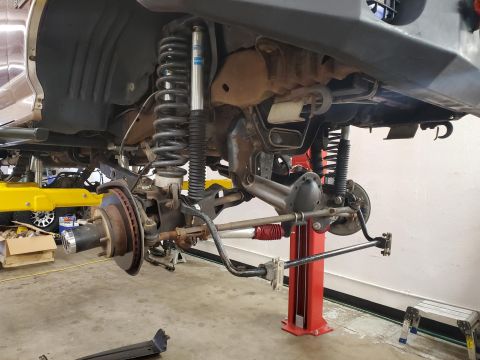 1996 Ford Bronco - Close-up view of a vehicle's front suspension and axle assembly, lifted for service, highlighting upgraded shocks and steering components.