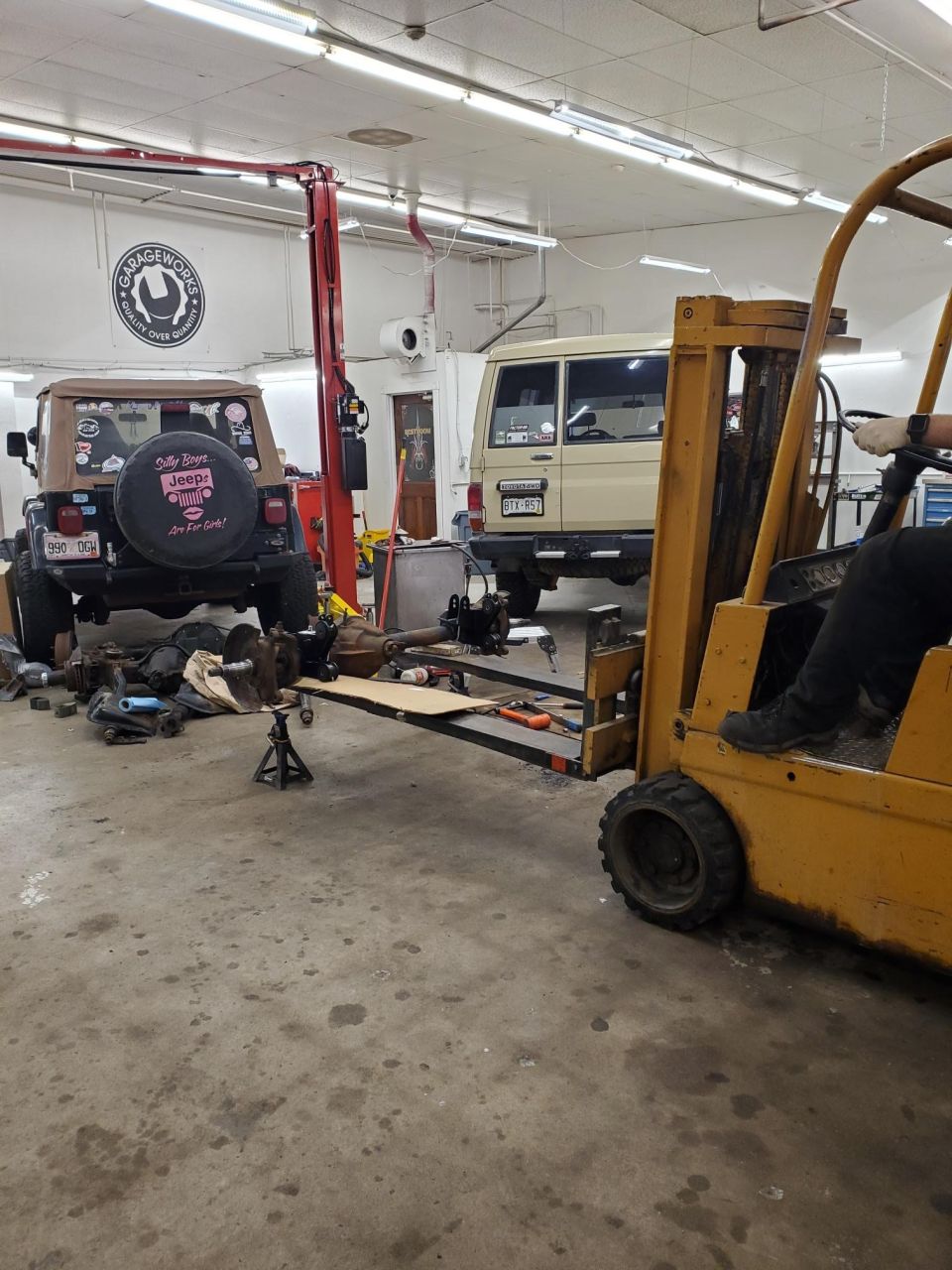 Jeep Wrangler rear with spare tire, disassembled axle on cart, and Toyota Land Cruiser in garage