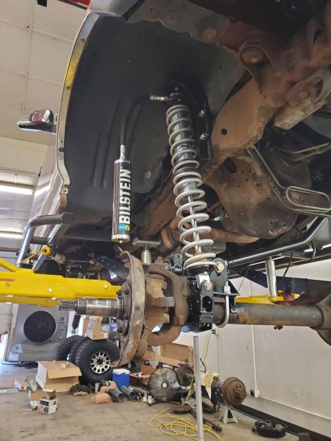 1996 Ford Bronco - Close-up of a vehicle's suspension system undergoing modification, showing a Bilstein shock absorber and coilover assembly.