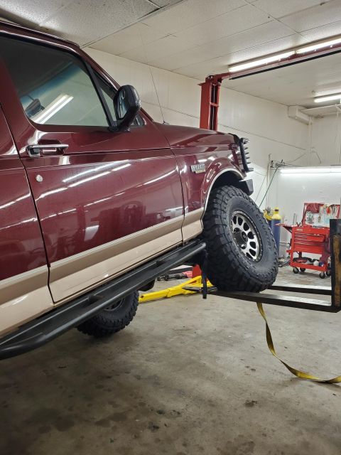 1996 Ford Bronco - A maroon Ford Bronco is shown on a lift in a garage, with its front tire elevated.
