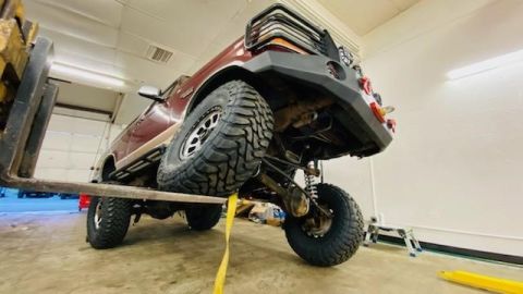 1996 Ford Bronco - A lifted 1996 Ford Bronco is being held by a forklift, revealing its custom suspension and off-road tires.