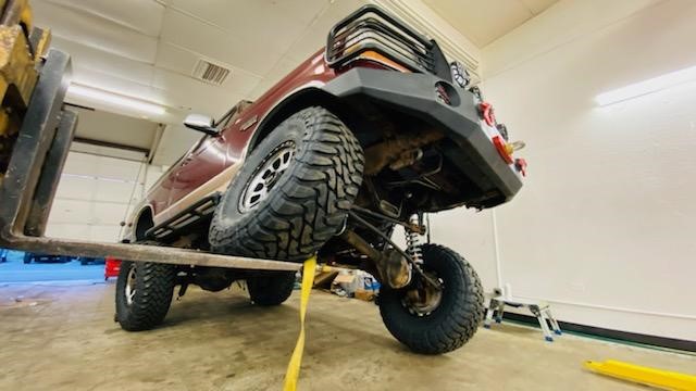 Red Ford Bronco lifted by a forklift, showing off its suspension and large tires