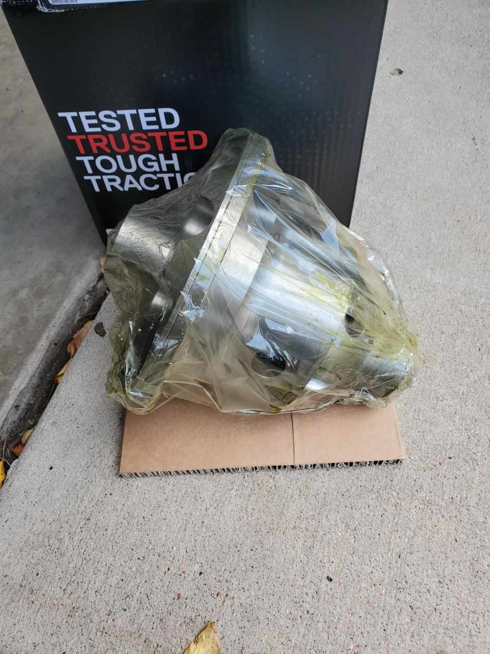 Differential part in plastic wrap on cardboard with "TESTED TRUSTED TOUGH TRACTION" box behind it