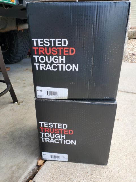 1996 Ford Bronco - Two boxes with "Tested Trusted Tough Traction" printed on them are stacked on a concrete surface, with a vehicle part in the background.