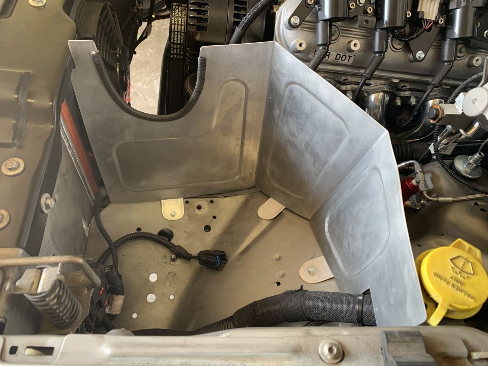 Engine bay with a metal shroud covering part of the engine. Wires and hoses are visible
