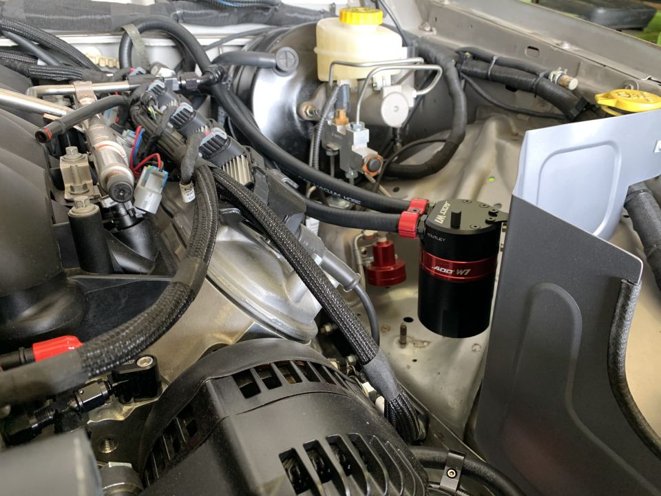 Engine bay with an oil catch can installed. Shows brake fluid reservoir and various hoses and wiring