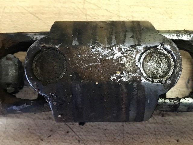 Greasy, corroded metal steering linkage component with two visible circular pivot points