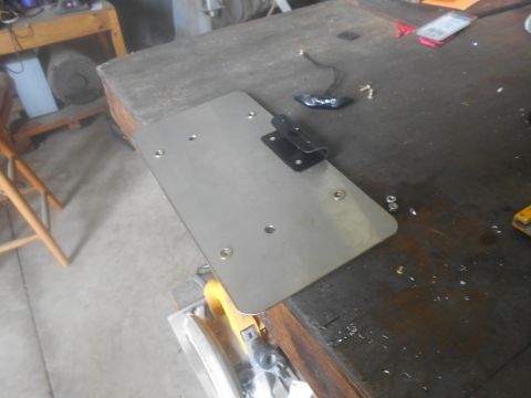 1992 Ford Bronco - A metal license plate bracket with an attached light is on a workbench, with tools and hardware scattered around.