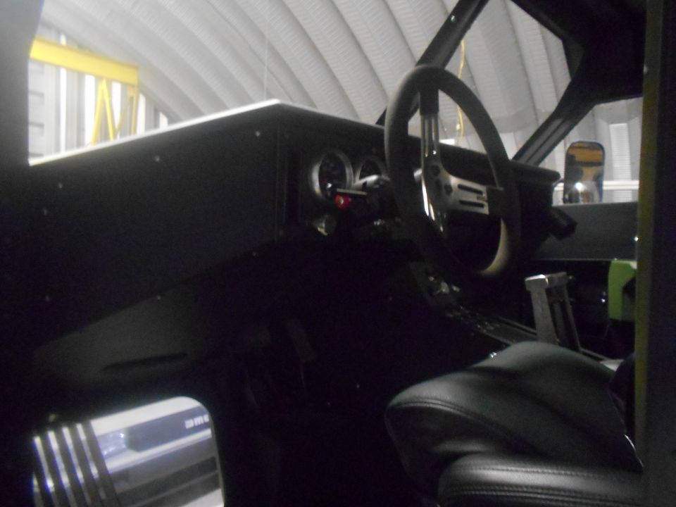 Interior view of a dark vehicle cabin, showing a steering wheel, dashboard gauges, and a gear shifter