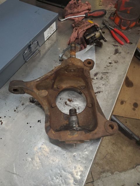 1996 Ford Bronco - A heavily rusted steering knuckle sits on a metal workbench, surrounded by various tools and rags.
