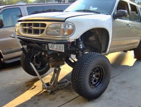 2000 Ford Explorer - A gold 2000 Ford Explorer SUV is shown with a white fender and lifted suspension, supported by a jack.