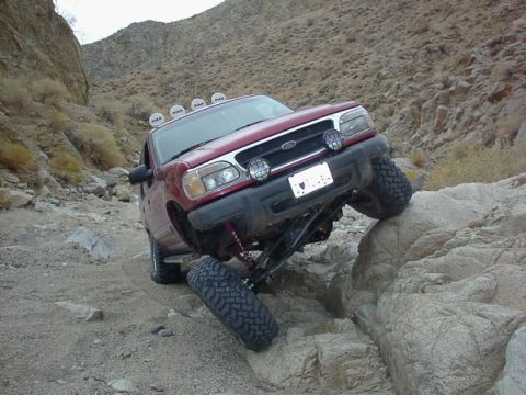 2000 Ford Explorer - A red 2000 Ford Explorer is shown off-roading over large rocks in a desert landscape.