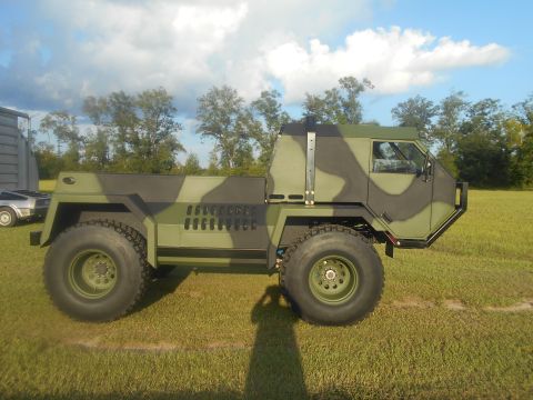 1992 Ford Bronco - A camouflaged military truck is parked on a grassy field under a cloudy sky.