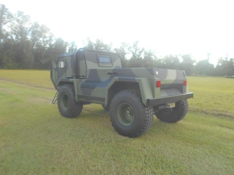 1992 Ford Bronco - This military truck, with its distinctive camouflage pattern, is viewed from a three-quarter front angle on a grassy field.
