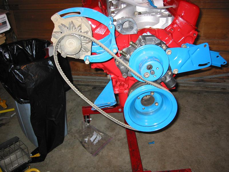 Red V8 engine on a stand with light blue pulleys, brackets and belt at the front