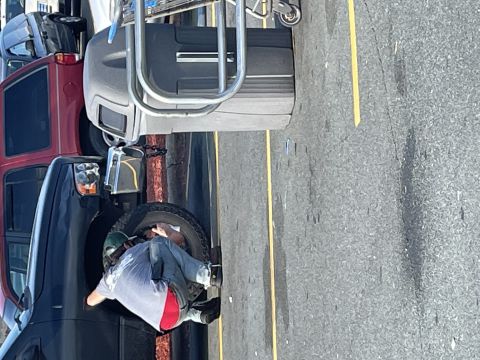2000 Isuzu Vehicross - A person works on a spare tire attached to the side of a dark SUV in a parking lot.