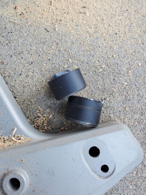 1996 Ford Bronco - Two rubber bump stops are shown on a gray plastic component, resting on a surface covered in sawdust.