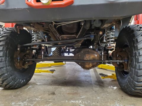 1996 Ford Bronco - The underside of a vehicle shows its front axle, steering components, and suspension system.
