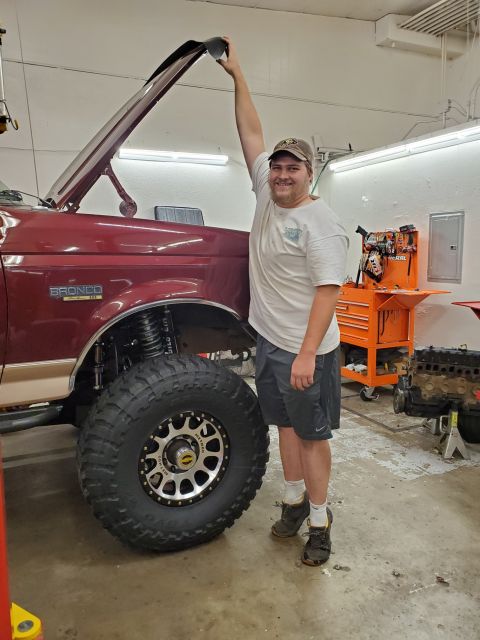 1996 Ford Bronco - A man stands next to a maroon 1996 Ford Bronco with its hood open, its lifted suspension and oversized tires.