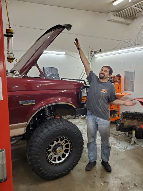 1996 Ford Bronco - A man stands next to a red 1996 Ford Bronco with a lifted suspension and oversized tires, possibly undergoing modifications.