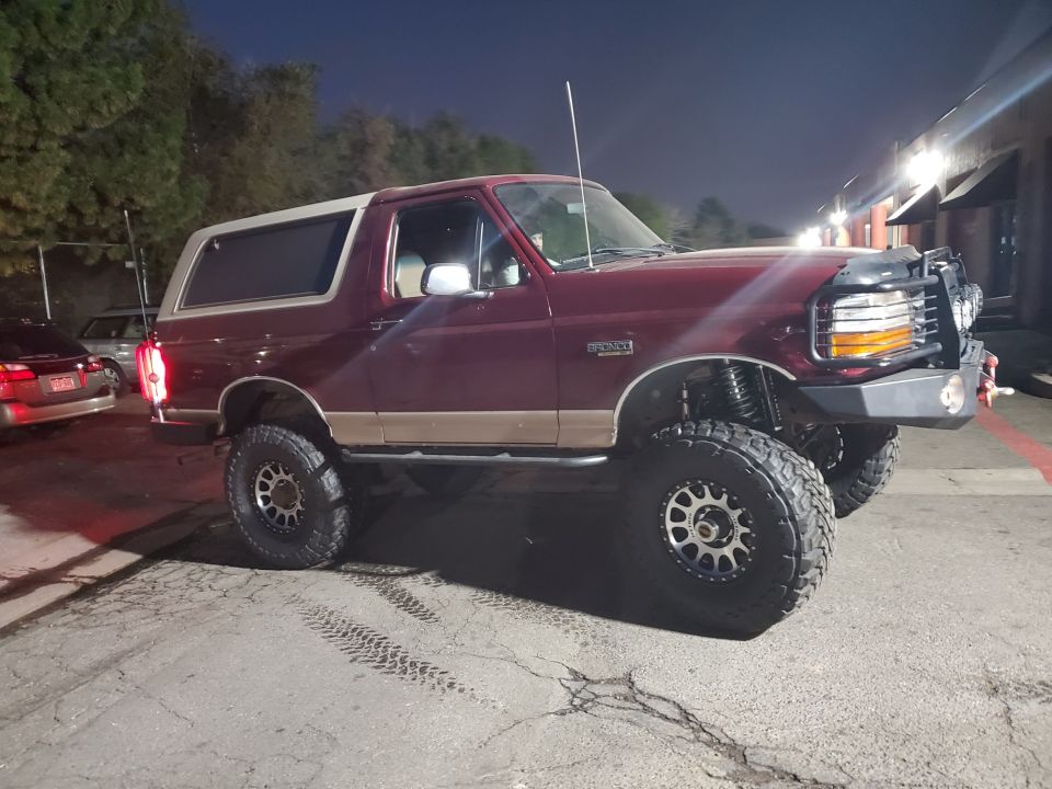 Maroon lifted Ford Bronco with tan trim, aftermarket bumper, and large tires