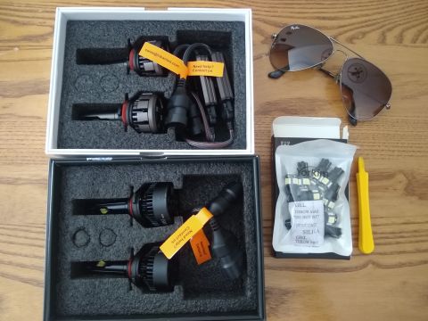 2008 Lexus LX 470 - Car parts, including LED headlight bulbs and smaller bulbs, are laid out with sunglasses and a tool on a wooden table.