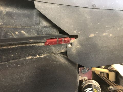 2014 Ford F-150 - Close-up view of vehicle undercarriage components, including red metal brackets and black trim, covered in dust.