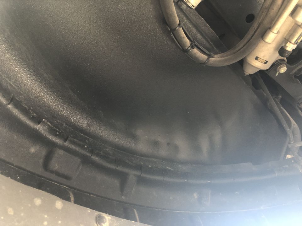 Close-up of a black plastic wheel well liner with some hoses and hydraulic lines visible above