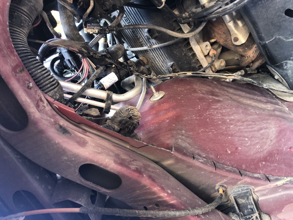 Close-up of engine bay wiring harness and metal tubing, with red painted metal body panels