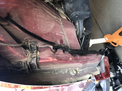 2014 Ford F-150 - The undercarriage of a red vehicle shows some damage and exposed wiring, with a jack visible.