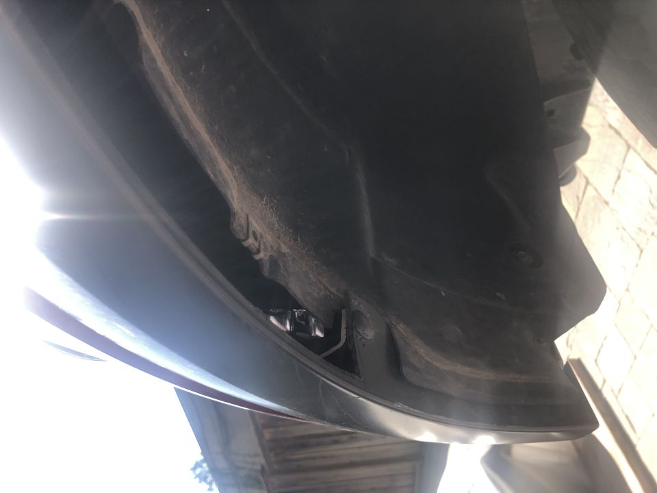 Underside view of a dark-colored vehicle's fender liner and wheel well area, showing dust and some mounting hardware