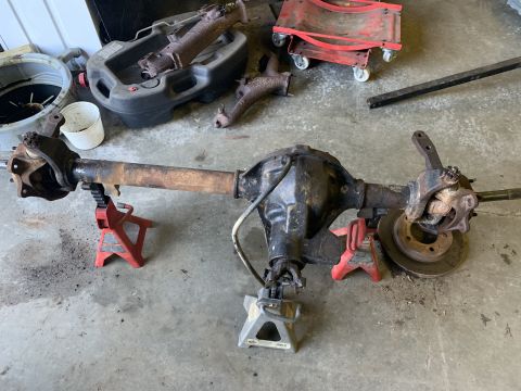 1979 Jeep CJ5 - A disassembled front axle assembly rests on jack stands in a garage, with various automotive parts scattered around.