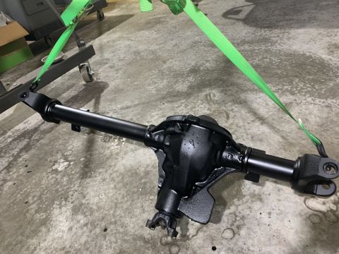 1979 Jeep CJ5 - rebuilt and black-painted solid axle housing with differential, secured by green ratchet straps on a concrete shop floor.
