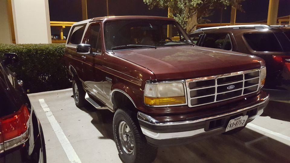 Maroon 1996 Ford Bronco with white roof, front passenger side view, parked at night.