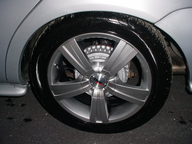 Silver car wheel with five spokes and a black tire. Brake caliper visible behind the wheel