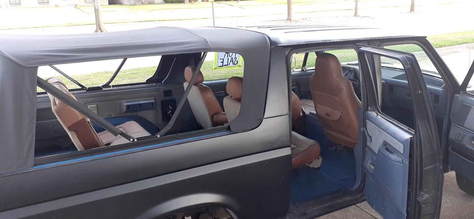Interior of a dark Ford Bronco with tan and brown seats and blue carpet.